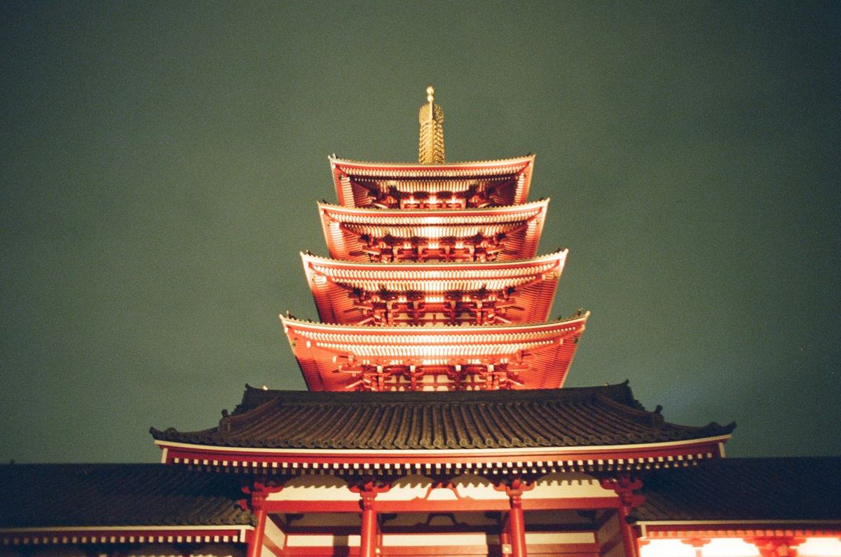A tiered temple lit warm orange against a dark green ground, its gold finial catching the light.