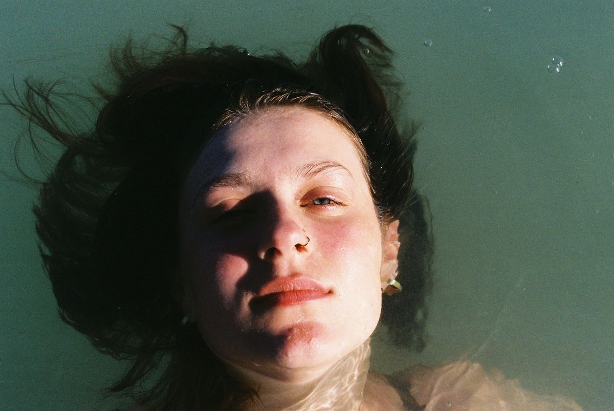 A close portrait of a face lit in teal and amber, hair loose and slightly blurred by motion.